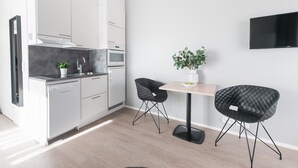 A modern kitchen with white cabinets, a black countertop, and a dining area with two black chairs and a table. - Forenom Serviced Apartments Helsinki Mansku (Helsinki)