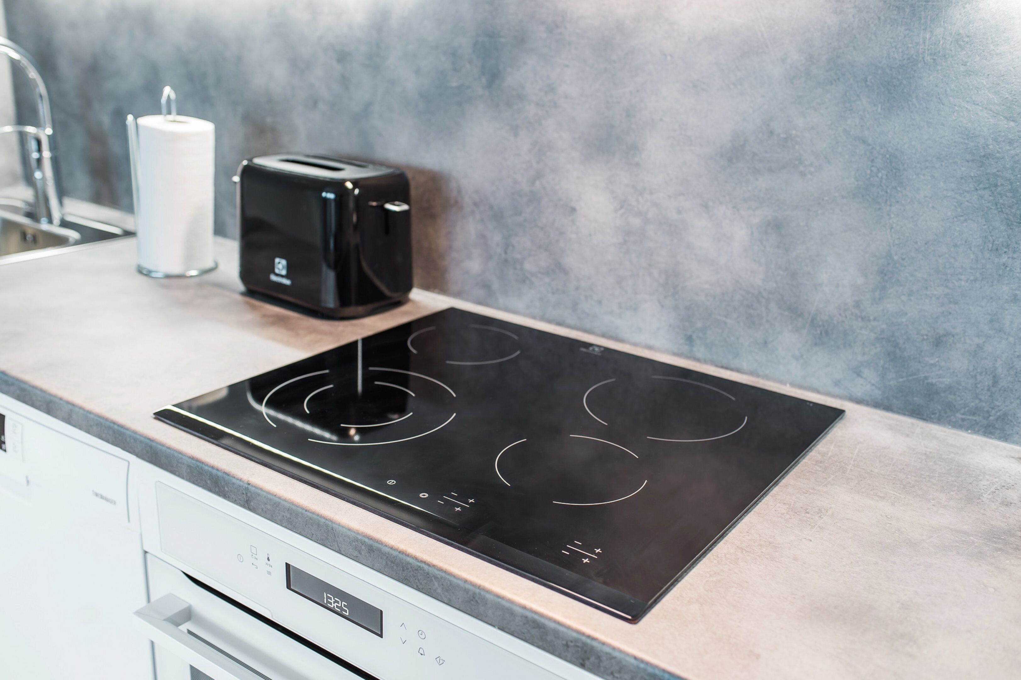 Una cocina con una placa de inducción moderna, un tostador y un dispensador de toallas de papel.
