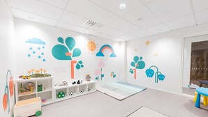 A child-friendly room with a play area, a white shelf with toys, and a large window. - Forenom Serviced Apartments Helsinki Mansku (Helsinki)