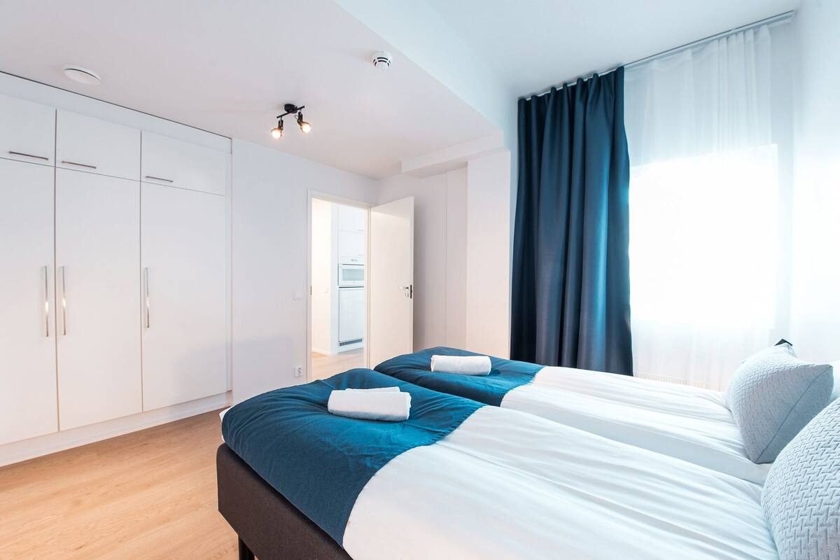 Een moderne hotelkamer met twee bedden, een kledingkast en een badkamer die door een open deur zichtbaar is.