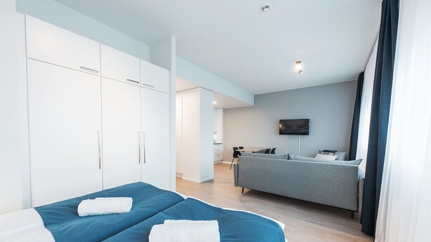A modern hotel room with two beds, a grey sofa, and a flat-screen TV. - Forenom Serviced Apartments Helsinki Mansku (Helsinki)