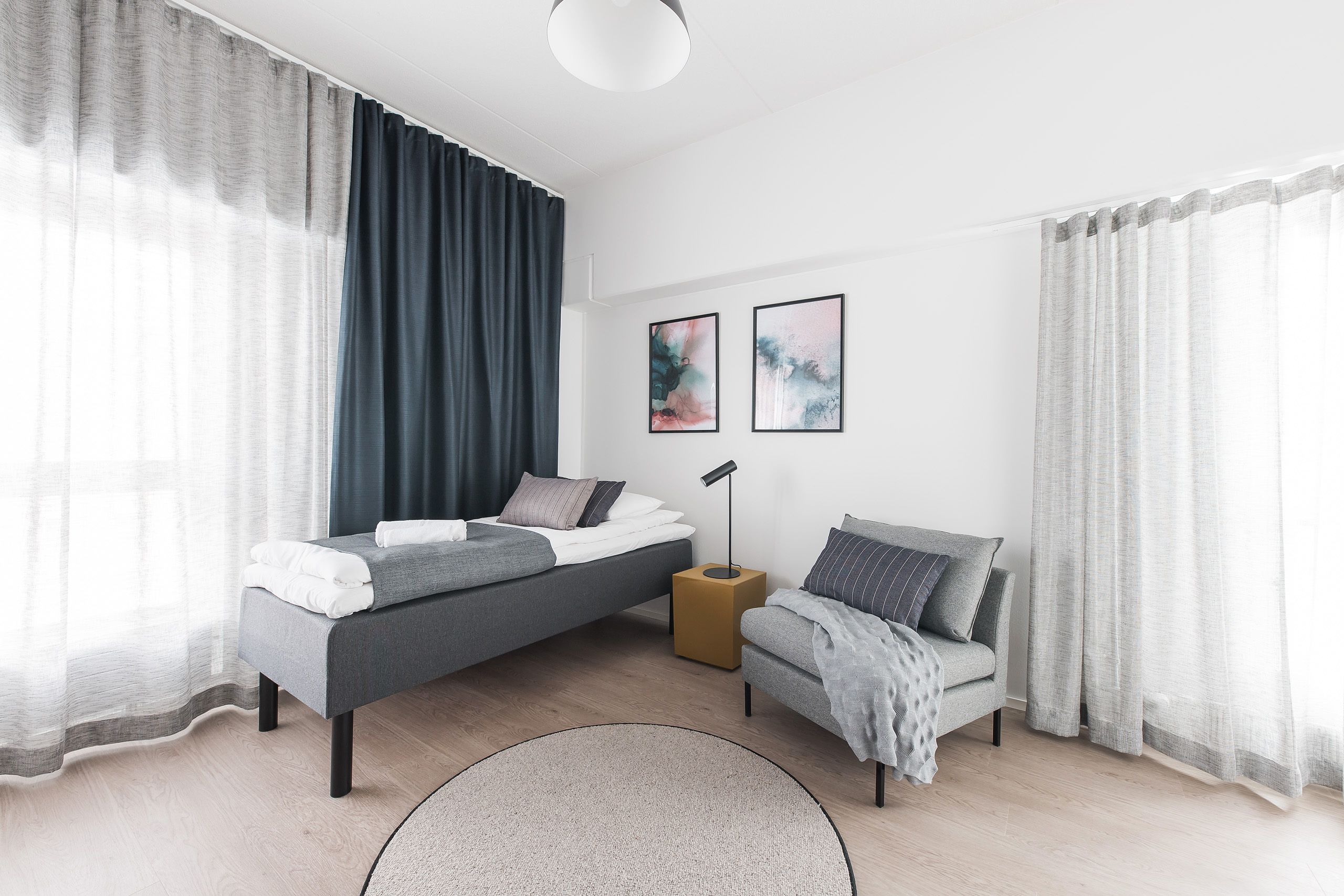 Un dormitorio moderno con una cama, un sofá, una mesita de noche y dos cuadros enmarcados en la pared.
