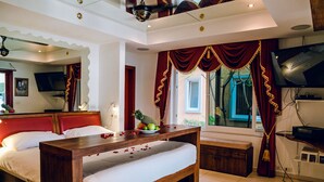Una habitación de hotel con una cama grande, un banco de madera, un televisor y una ventana con cortinas.