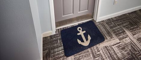 A grey door with a wreath, a doorbell, and a doormat with an anchor symbol.
