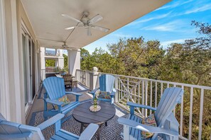 A balcony with blue Adirondack chairs, a round table with a bottle and glasses, and a ceiling fan. - BEACHFRONT BUILDING l PRIVATE BEACH l FREE SEASONAL BEACH SETUP (Santa Rosa Beach)