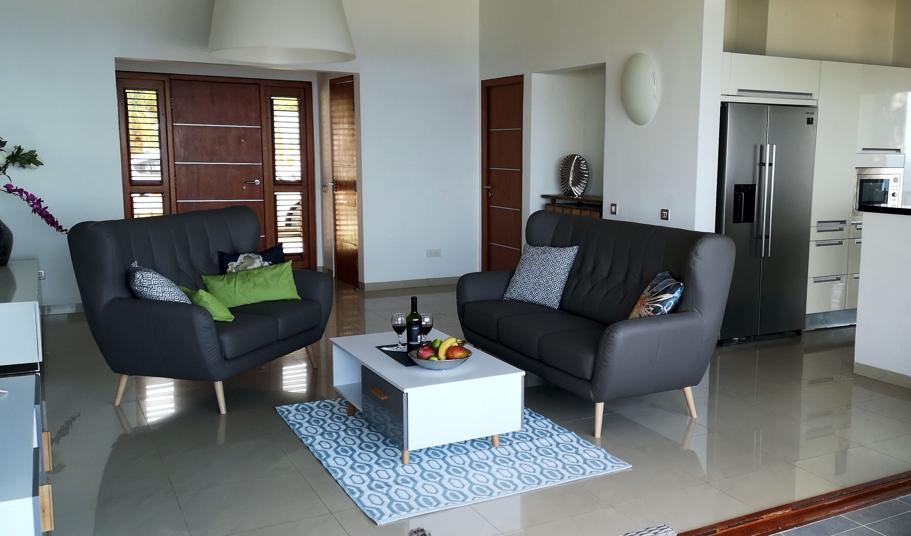 A modern living room with two black sofas, a white coffee table, and a patterned rug.