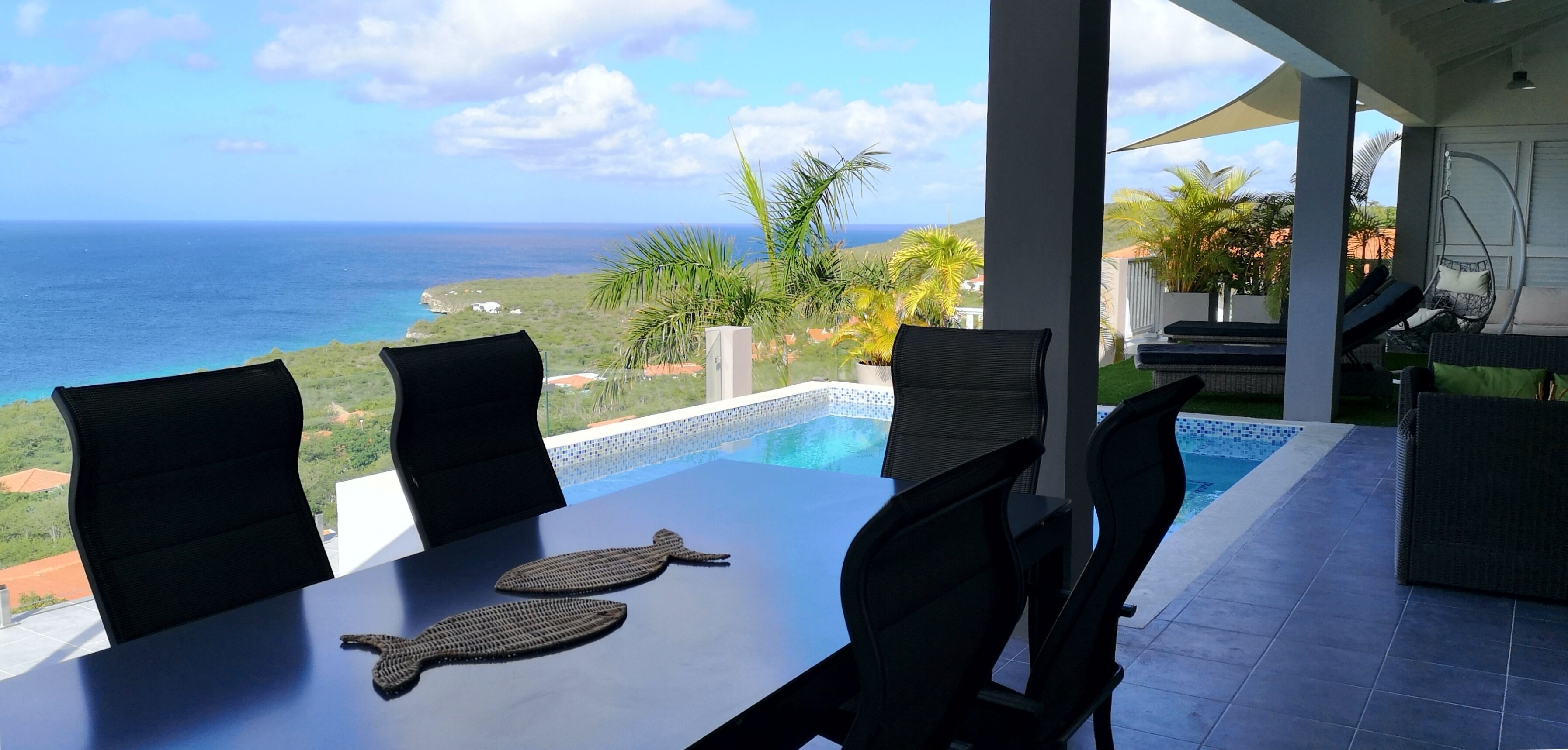Un área de comedor con vista al océano, una piscina y mobiliario exterior.
