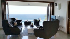 Una sala de estar con vista al océano, dos sofás, una mesa de centro y un televisor.