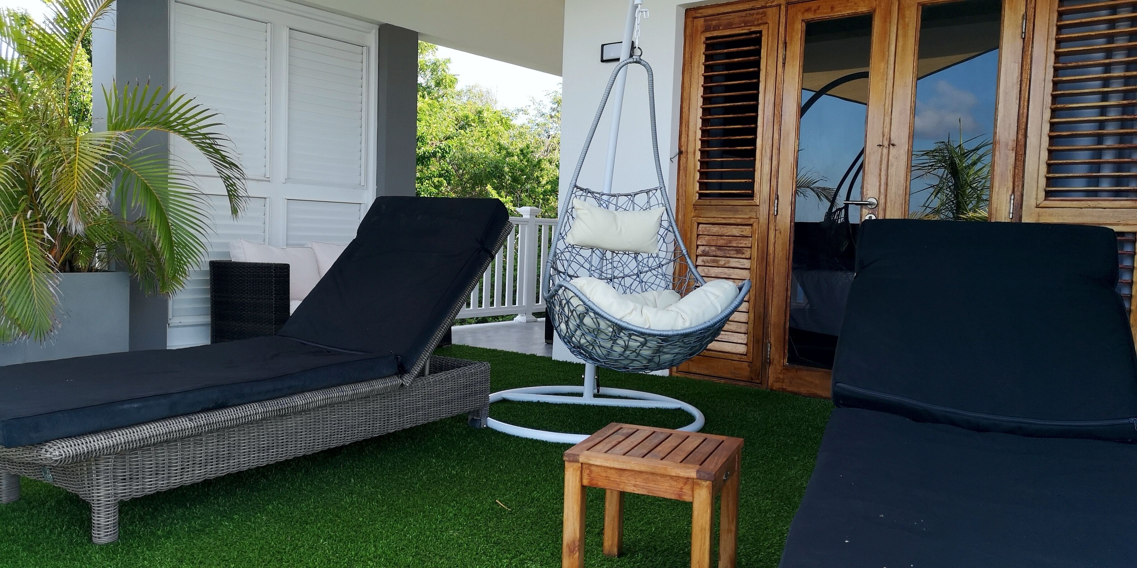Un patio con una silla de mimbre, una mecedora colgante y un taburete de madera.