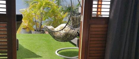 A bedroom with a bed, two towels, a view of a garden, and a hammock.