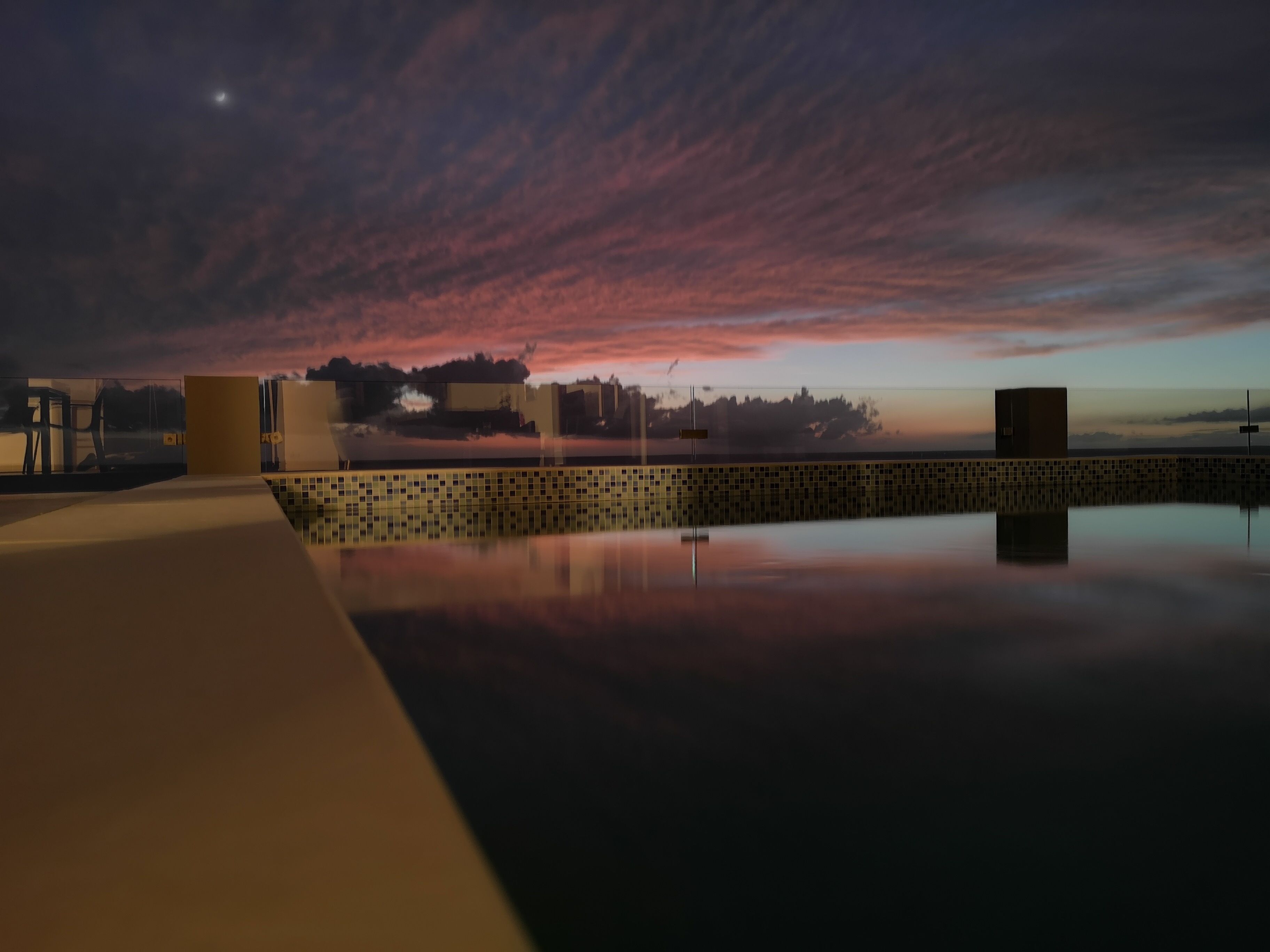 A rooftop pool with a view of a sunset and city skyline.