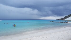Una playa con agua turquesa cristalina, una orilla arenosa y un promontorio rocoso en la distancia.