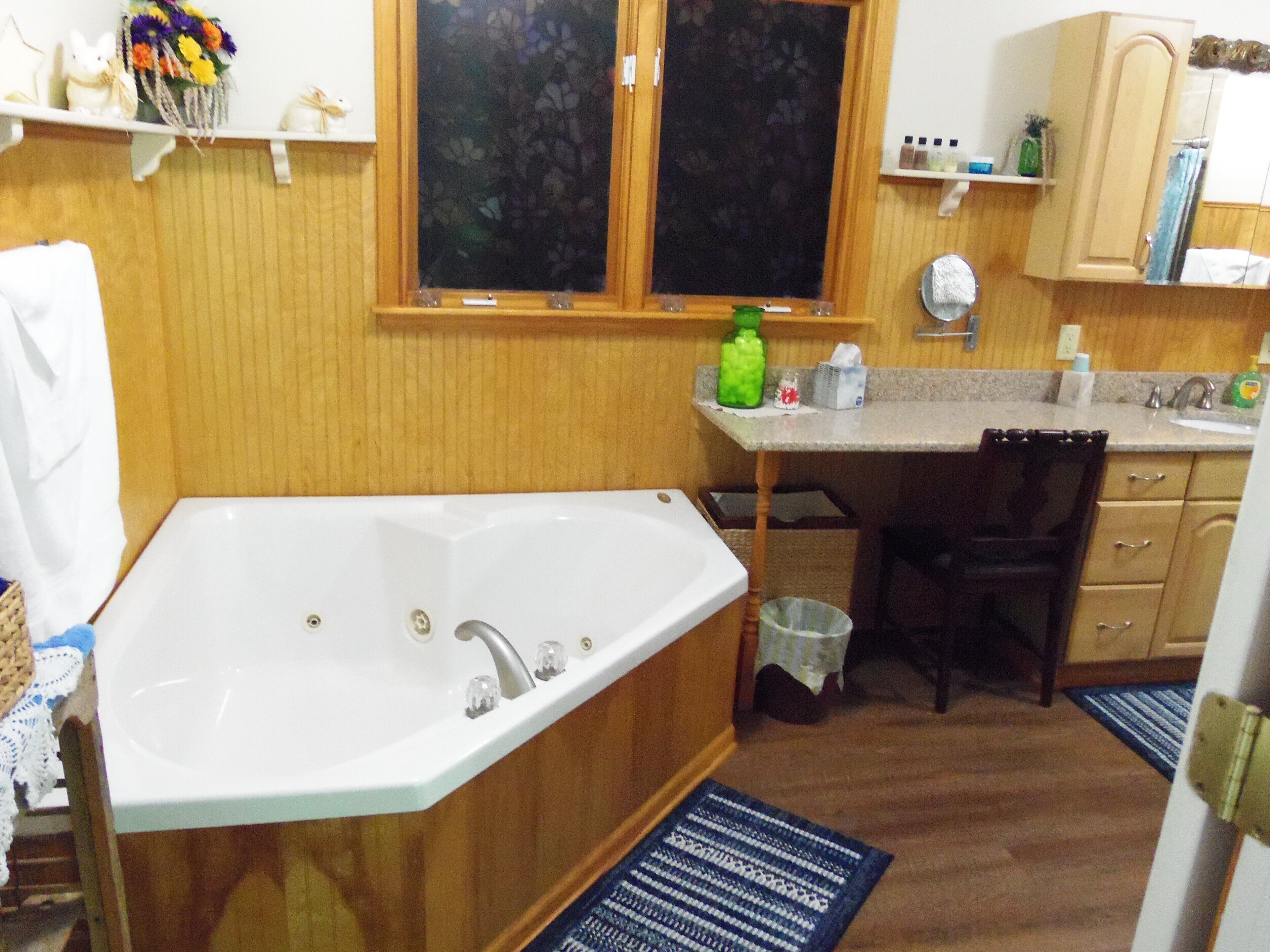 Casa de banho com banheira, lavatório e janela. Há uma prateleira com artigos de higiene e um cesto de lixo.