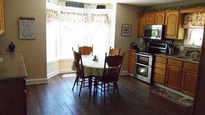 Una cocina con armarios de madera, microondas, horno y una mesa de comedor con sillas.