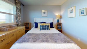 Une chambre à coucher bien rangée, avec un lit, une commode, une table de chevet, une lampe et des tableaux encadrés accrochés au mur.