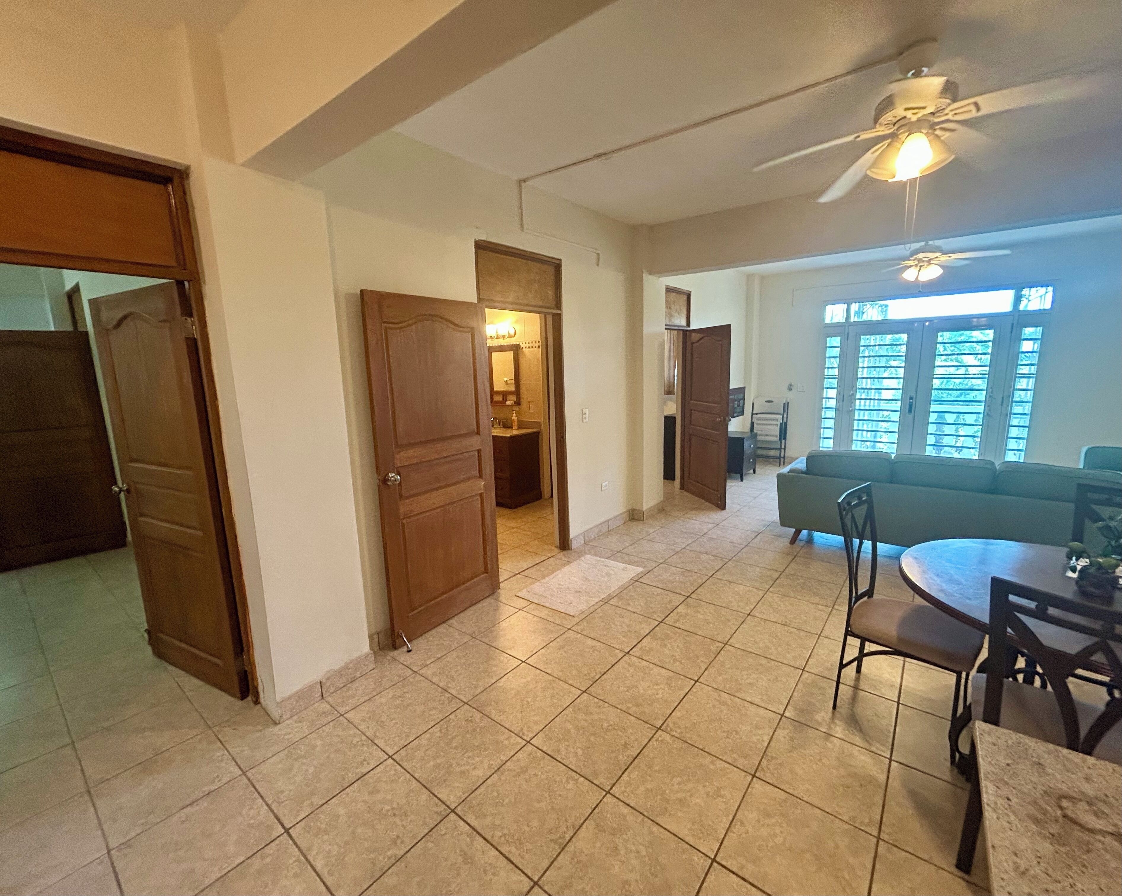 Uma sala de estar ampla com uma mesa de jantar, cadeiras, sofá e ventilador de teto.