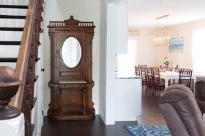 A staircase with a wooden handrail, a wooden cabinet with a mirror, and a dining area with a white table and chairs. - Spacious Victorian Main House with Luxury Kitchen in Beautiful Historic District (Ocean City)