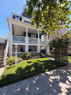 A two-story residential building with a balcony, a well-maintained lawn, and a clear sky.