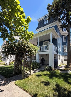 A two-story house with a covered porch and a small garden. - Spacious Victorian Main House with Luxury Kitchen in Beautiful Historic District (Ocean City)