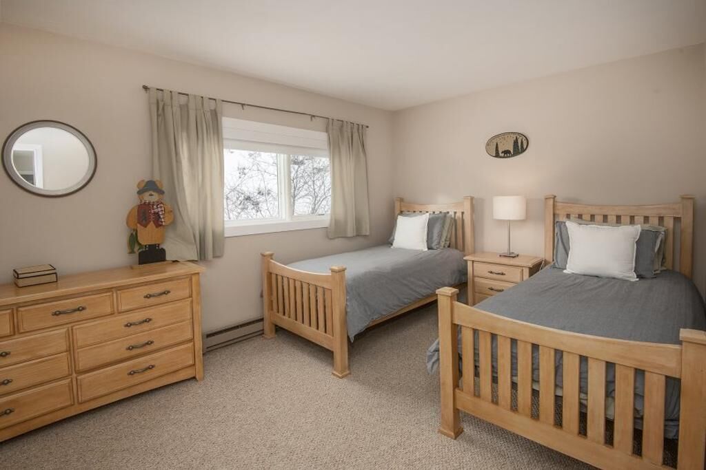 Une chambre avec deux lits en bois, une commode, une table de chevet avec une lampe, une fenêtre avec des rideaux et un miroir sur le mur.