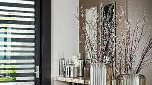 Een moderne eetruimte met een glazen tafel, metalen vazen en een kroonluchter.