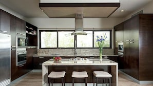 Een moderne keuken met donkerhouten kastjes, roestvrijstalen apparatuur, een marmeren aanrechtblad en een groot raam dat voor natuurlijk licht zorgt.