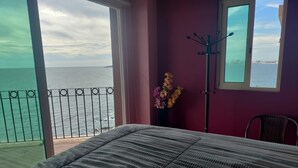 Un dormitorio con cama, ventana, silla, perchero y vista al mar.