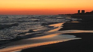 A beach at sunset with waves, a clear sky, and distant buildings. - #404- 2 bed-1 bath sleeps 6- Fall beach getaway…& Winter Snowbirds! Book now! (Gulf Shores)