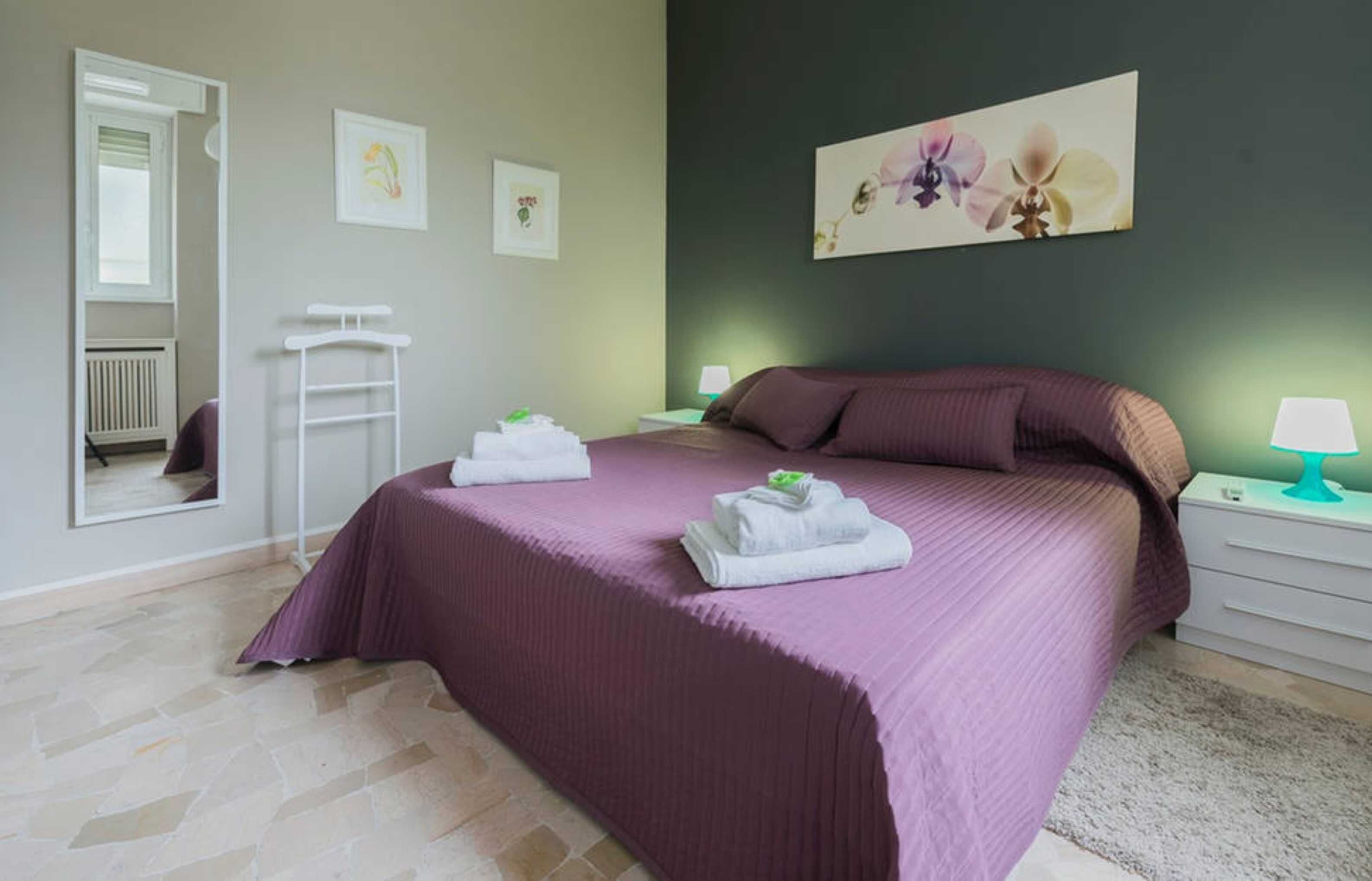 A bedroom with a large bed, a white radiator, a white towel rack, and a green wall with a floral painting.