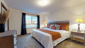 Une chambre d’hôtel avec un grand lit, deux tables de chevet avec des lampes, une fenêtre avec des rideaux et une vue sur les bâtiments environnants.