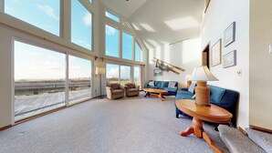 Un salon spacieux doté de grandes fenêtres, d’un canapé bleu, de deux fauteuils, d’une table basse en bois et d’une lampe.