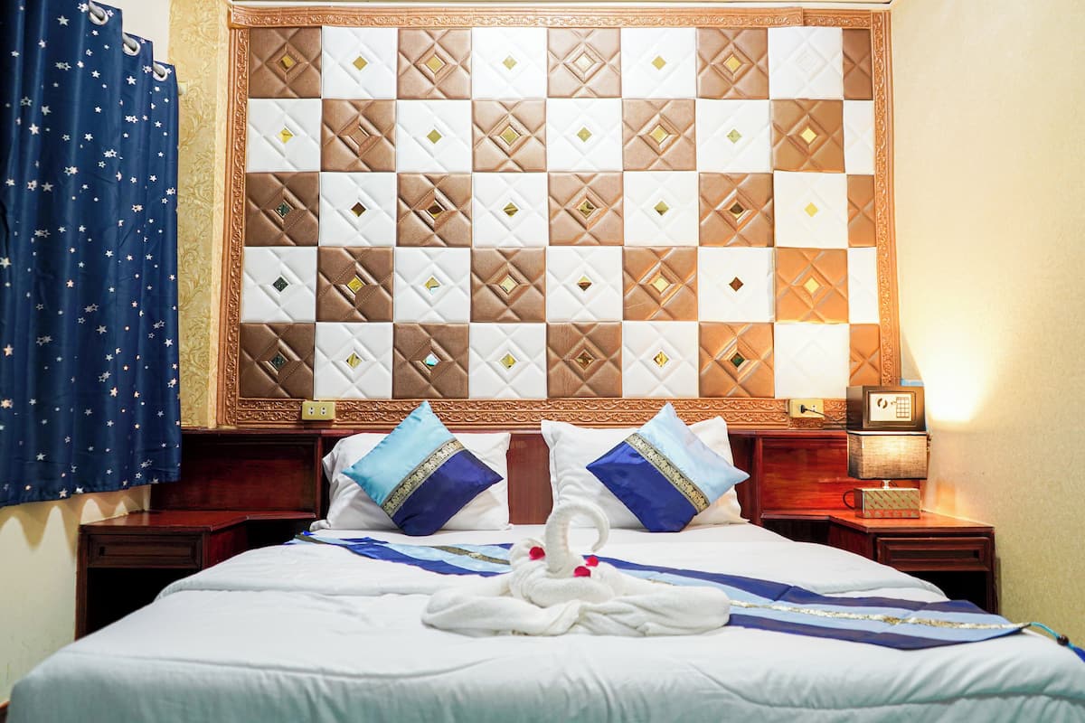 A hotel room with a large bed, a headboard with a quilted pattern, two nightstands, and a blue curtain with star patterns.