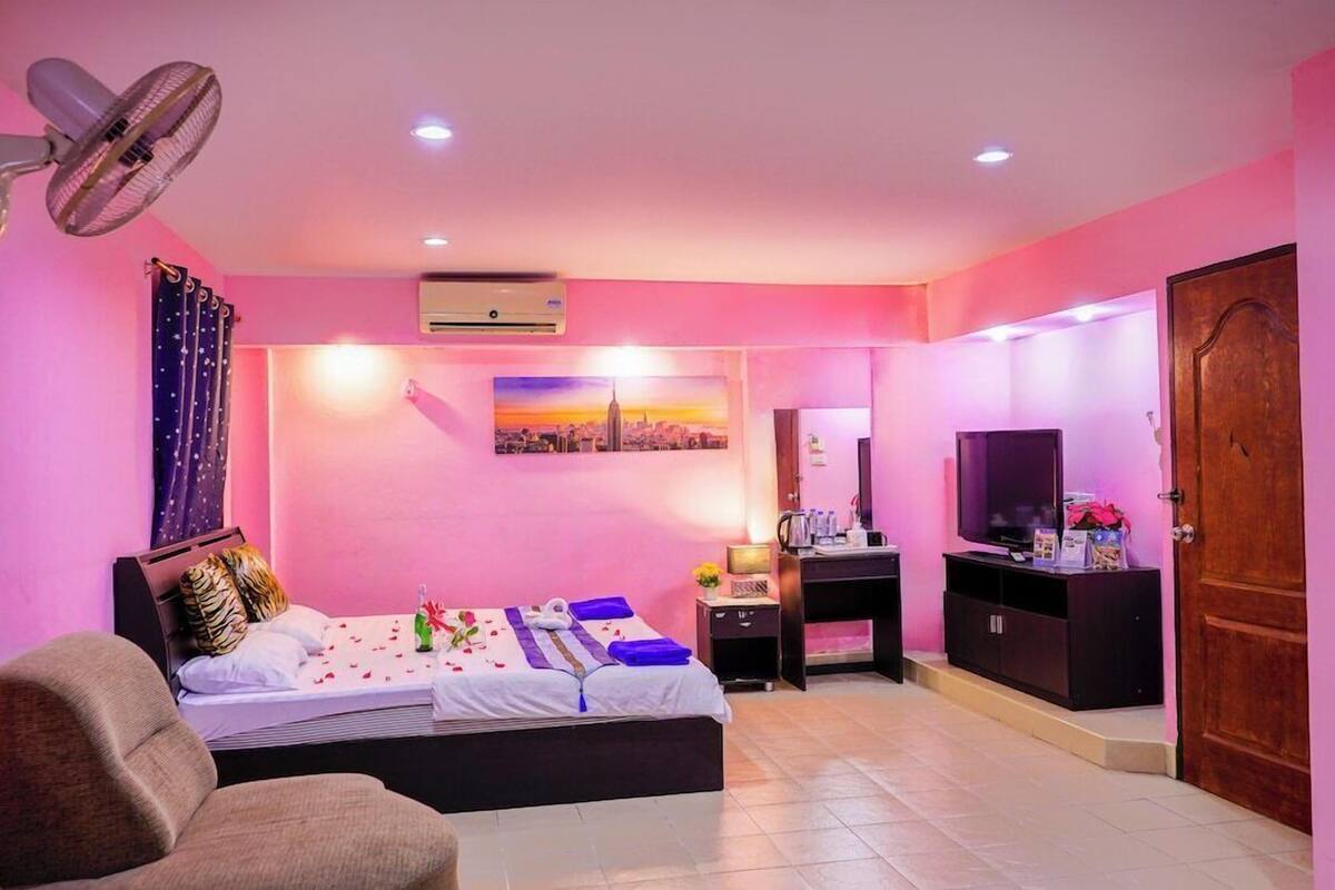 A bedroom with a bed, a desk, a TV, and a fan.