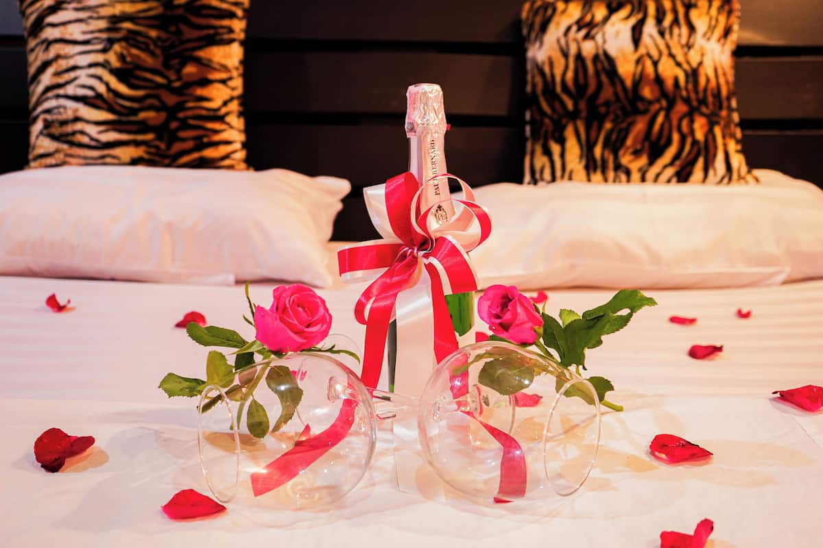 A bed with rose petals, a champagne bottle, and two glass bottles with roses.