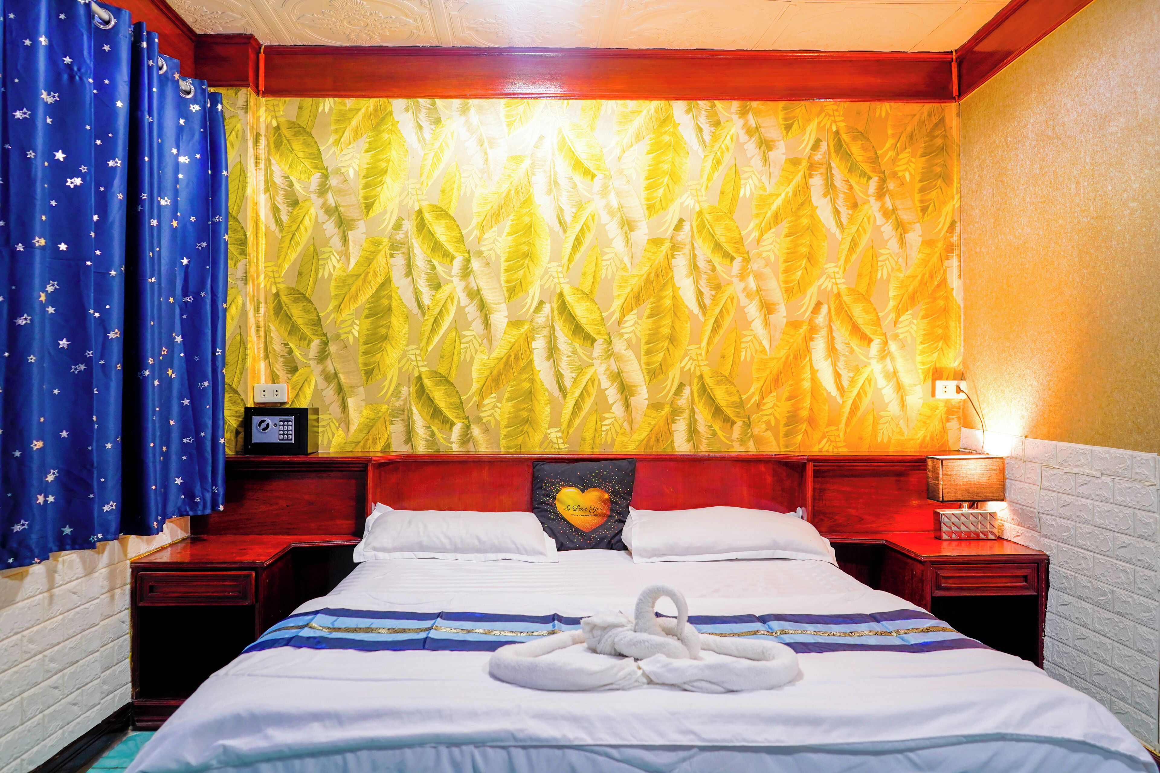 Une chambre d’hôtel avec un lit, une table de chevet, une horloge murale et un mur orné d’un motif de feuilles.