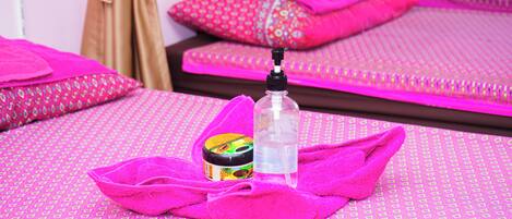 A hotel room with pink patterned bedsheets, a bottle of lotion, and a pink towel.