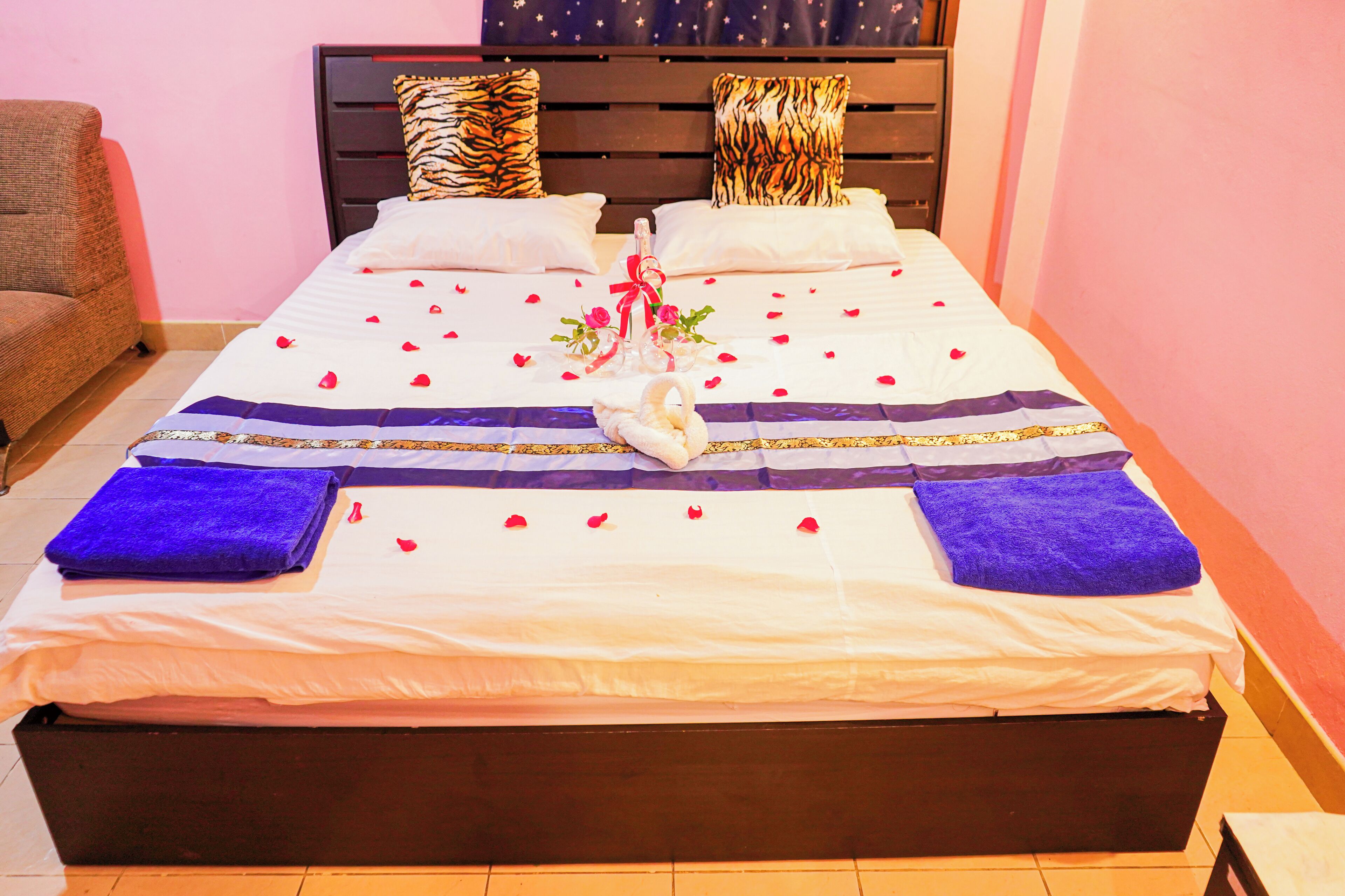 Una cama bien hecha con un adorno decorativo, un cabecero de madera y una silla en una habitación con paredes rosas.