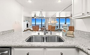 A kitchen with a double sink, granite countertop, and a view of the ocean.