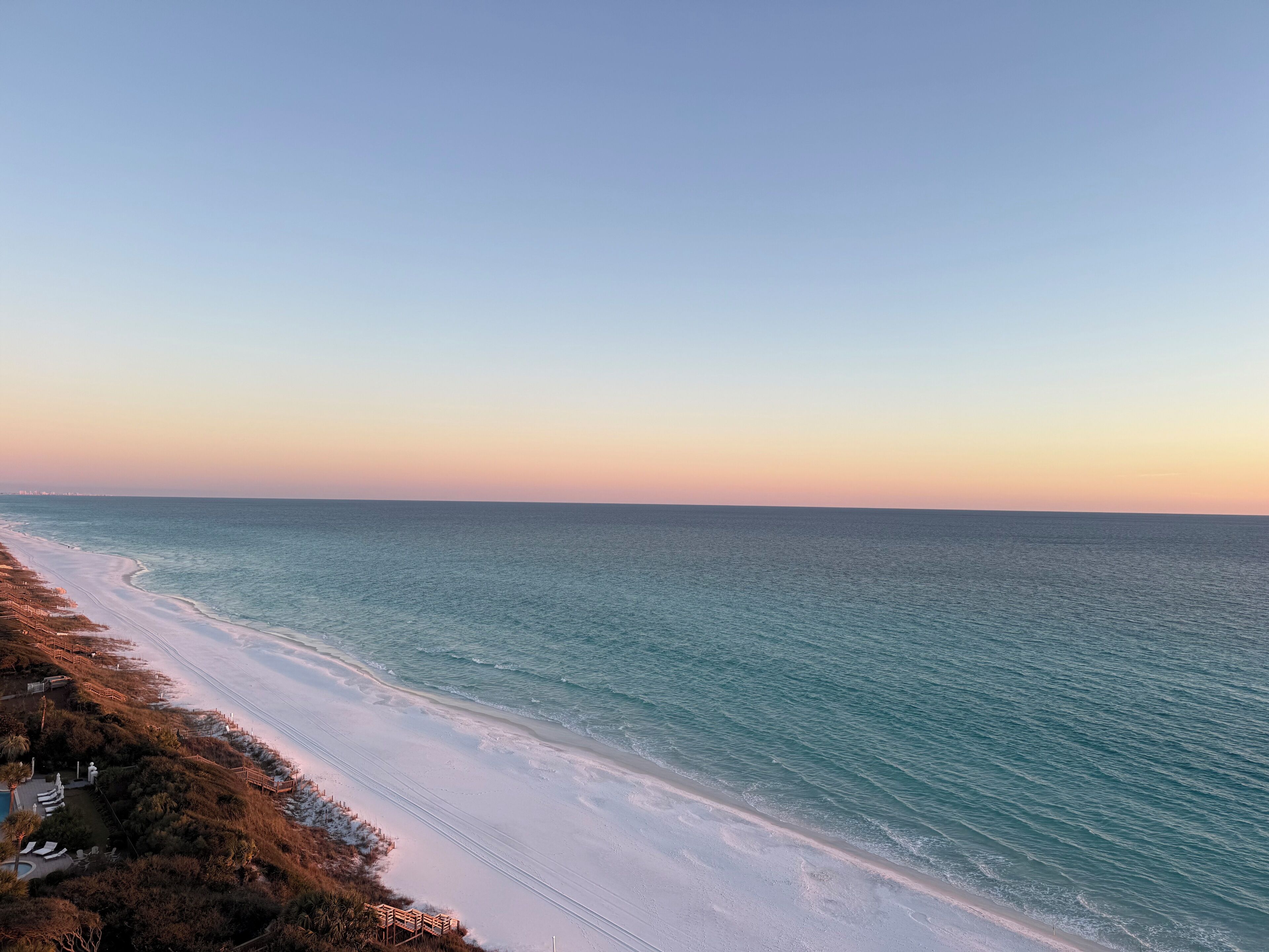 A beach with a clear sky, a sandy shoreline, and a wooden walkway.