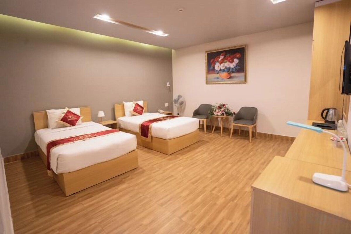 A hotel room with two beds, a desk, a chair, and a television.