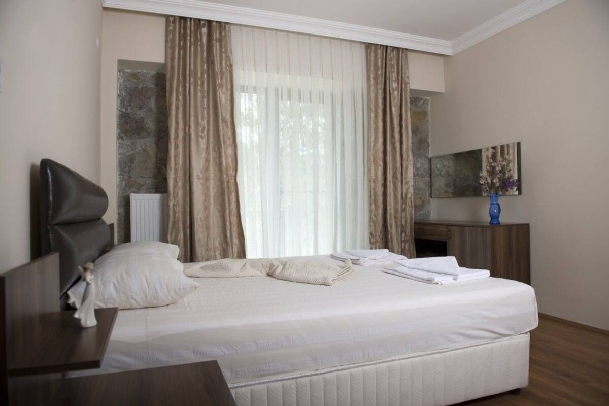 A hotel room with a large bed, a nightstand, a dresser, and a window with curtains.