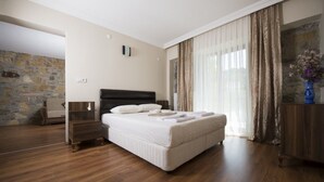Un dormitorio con una cama grande, suelo de madera, pared de piedra y vistas al exterior.