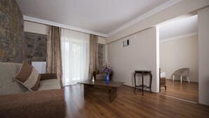 Una sala de estar con pared de piedra, suelo de madera, sofá, mesa de centro, una silla y una pequeña mesa con un florero.