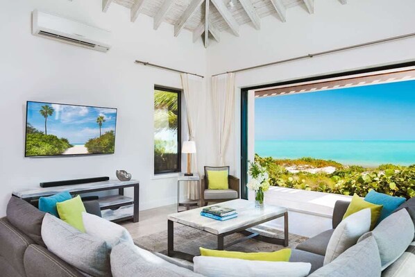 Ein modernes Wohnzimmer mit großem Fenster und Blick auf das Meer, einem wandmontierten Flachbildfernseher und einer gemütlichen Sitzecke mit Couchtisch.