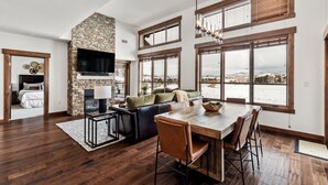 A spacious living area with a stone fireplace, large windows, and a dining table. - Top-Floor Luxury Condo with Panoramic Views at Trailhead Lodge! (Steamboat Springs)