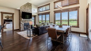 A spacious living room with a stone fireplace, large windows, and a dining area. - Top-Floor Luxury Condo with Panoramic Views at Trailhead Lodge! (Steamboat Springs)