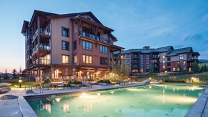 A multi-story hotel with a swimming pool, outdoor seating, and a well-lit patio area. - Top-Floor Luxury Condo with Panoramic Views at Trailhead Lodge! (Steamboat Springs)