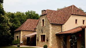 Un edificio de piedra con techo de tejas, un patio cubierto y un pequeño jardín.