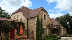Una casa de piedra con techo de tejas, un patio con mesa y sillas, y una puerta roja.