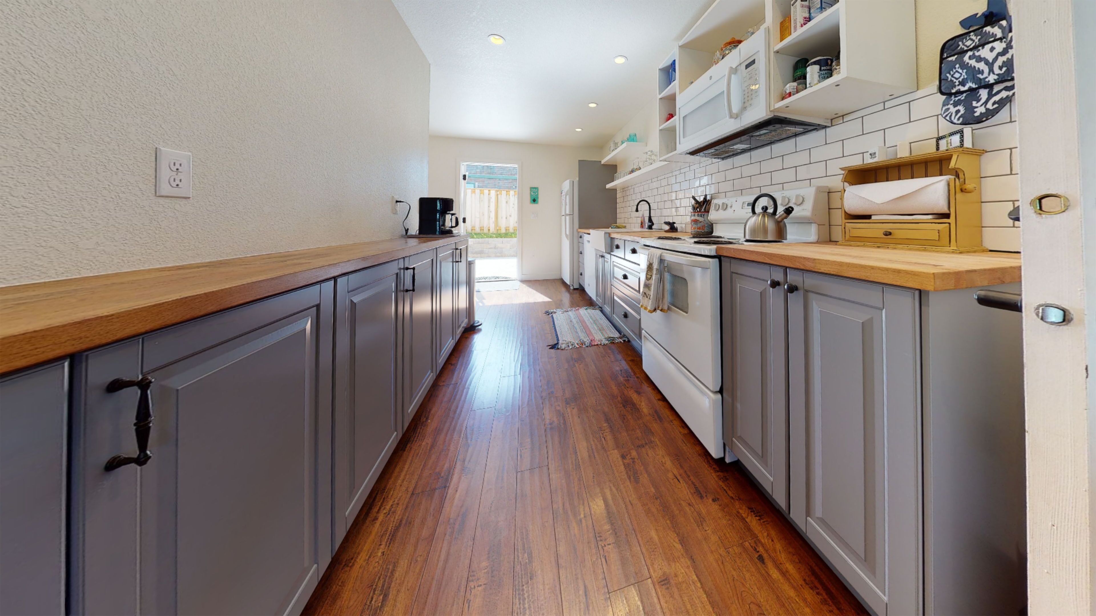 Una cocina estrecha con gabinetes grises, encimeras de madera y un salpicadero de azulejos.